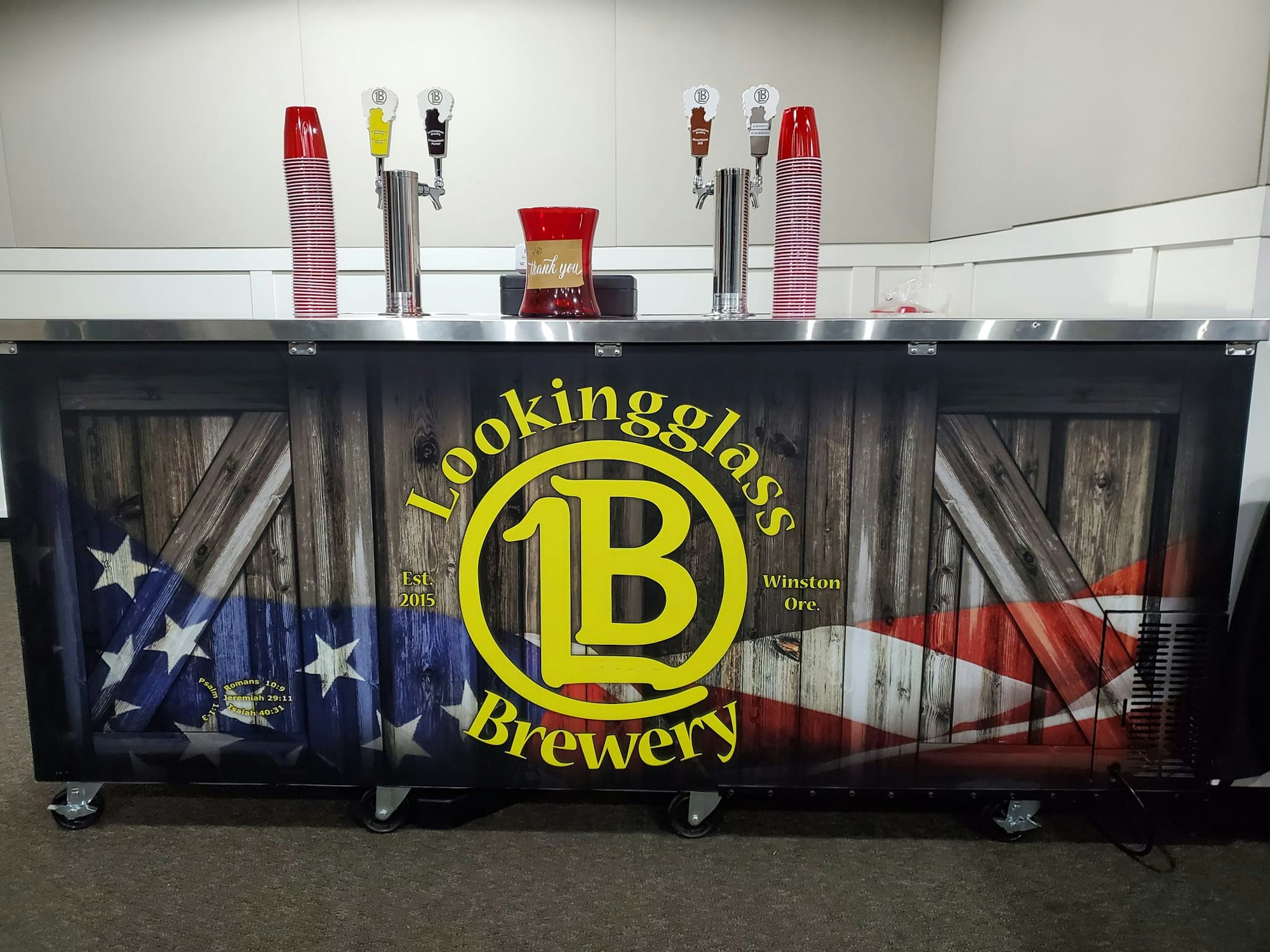 The image shows a brewery bar with taps, red cups, and a design featuring a rustic theme and the name "Lookingglass Brewery" from Winston, Oregon.