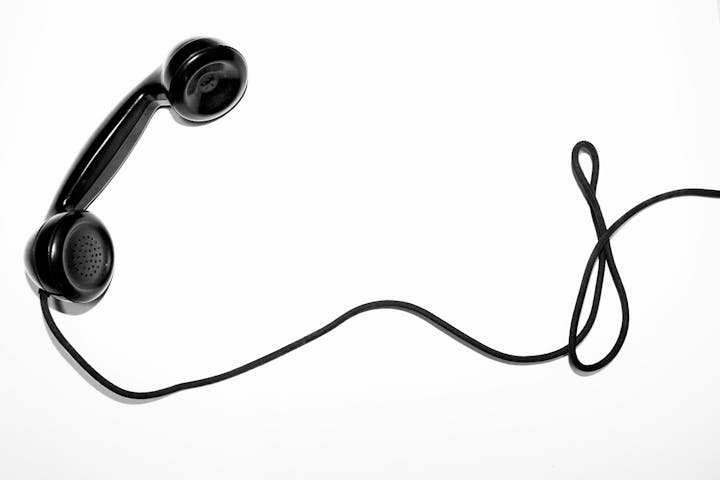 A black telephone handset with a coiled cord on a white background.