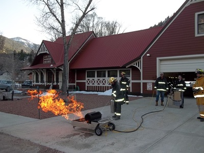 Firefighters training with a live fire in front of a building.