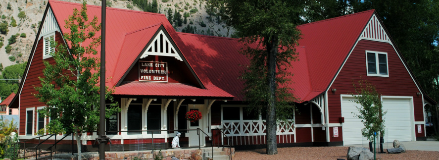 Red-roofed building labeled "Lake City Volunteer Fire Dept." with trees and a clear sky.