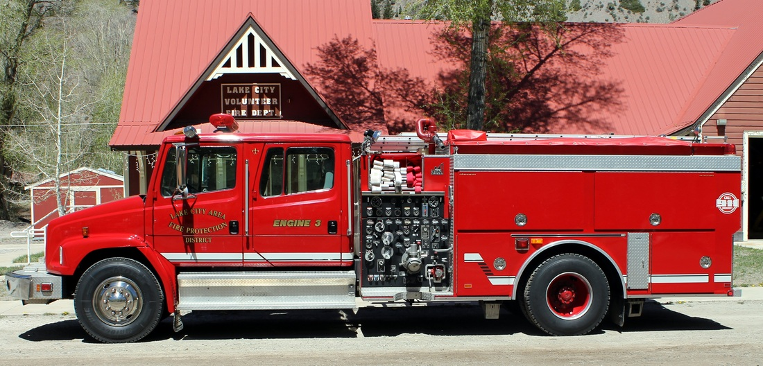 A red fire engine parked in front of a building with "Lake City Volunteer Fire Dept." sign.