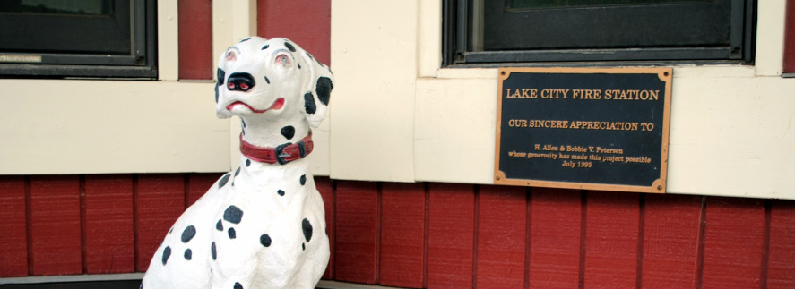 A Dalmatian statue outside a fire station with an appreciation plaque.