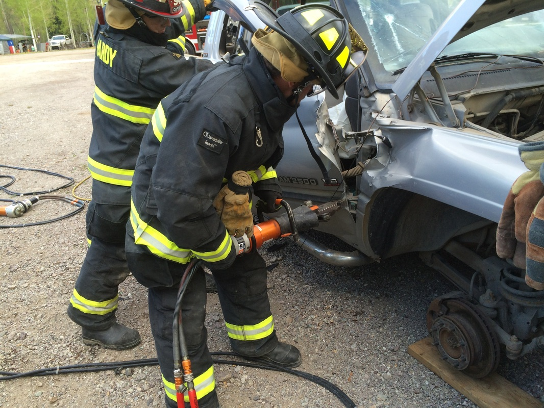 Firefighters using hydraulic tools on a damaged car during a rescue training exercise.