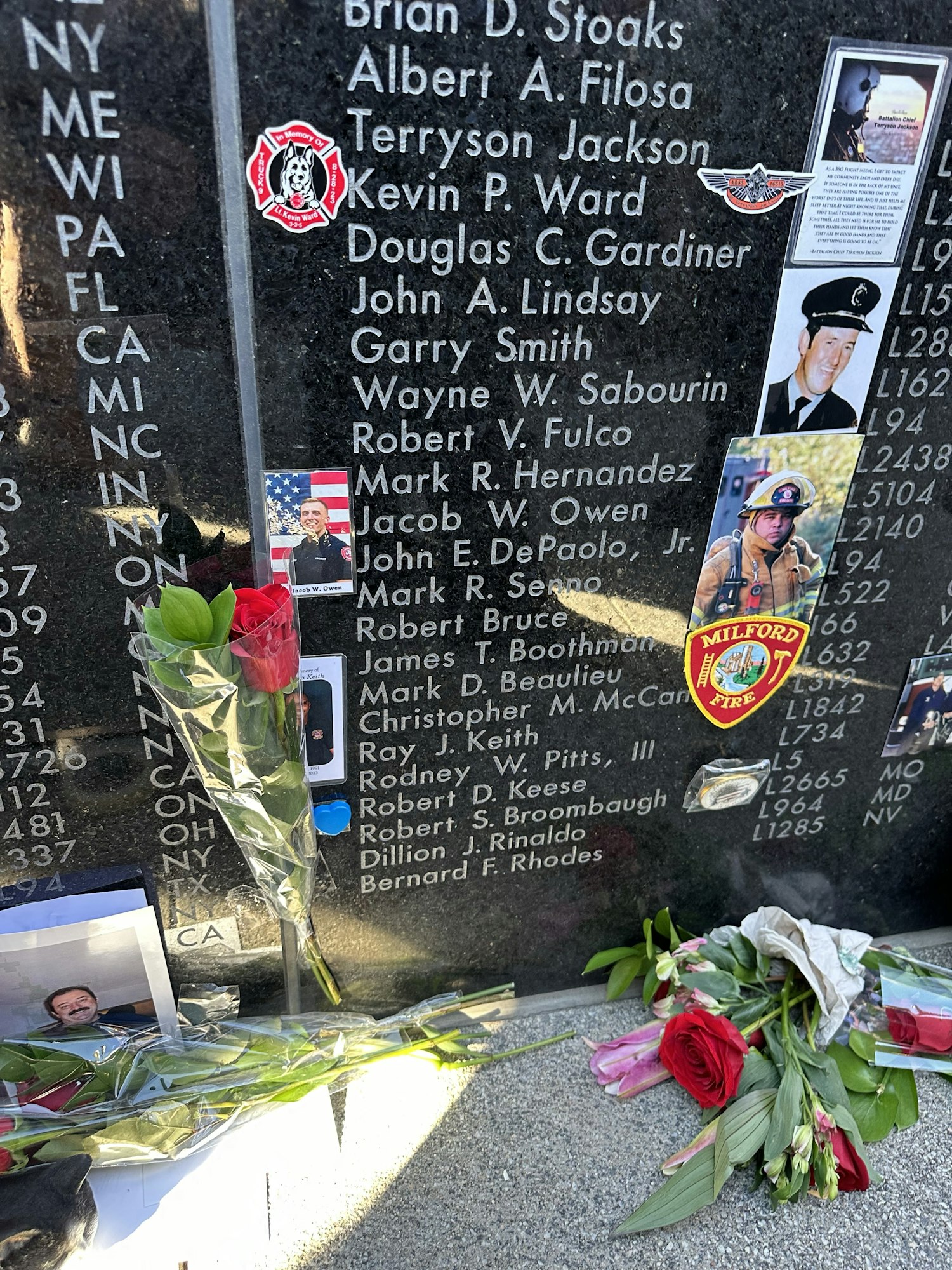 Memorial wall with names, firefighter emblem, flowers, and tribute photos.