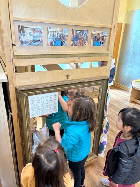 Children interacting with a mirror, looking at a chart with various facial expressions.