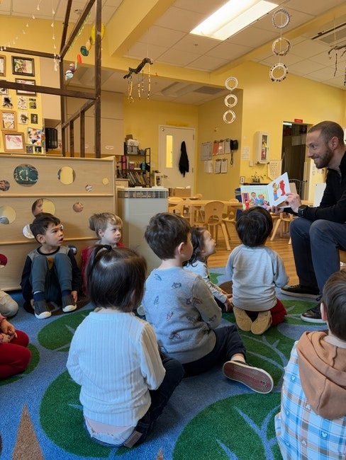 A teacher reads to a group of children seated on a carpet in a classroom.