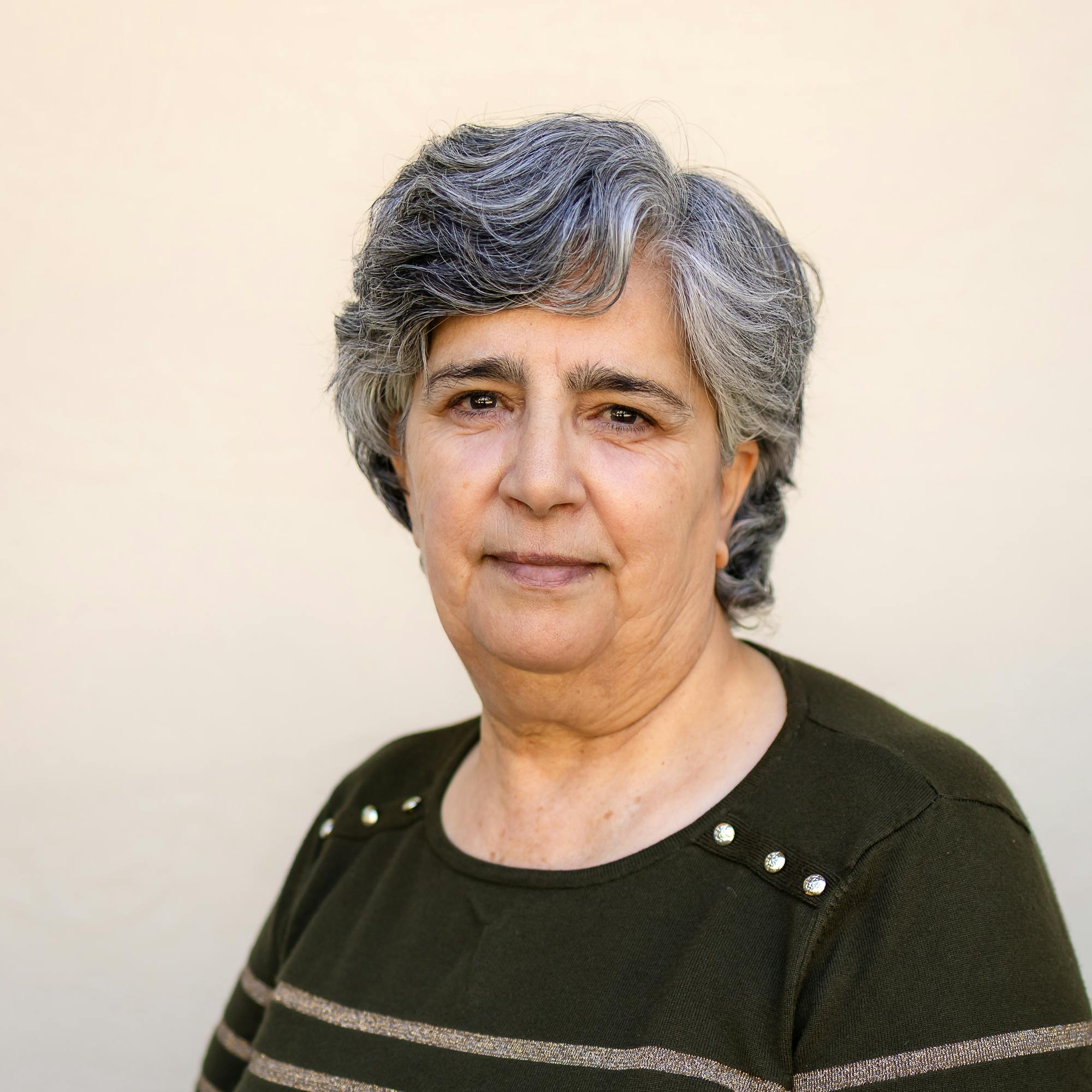 A woman with gray hair wearing a green striped top poses against a light background, giving a gentle smile.