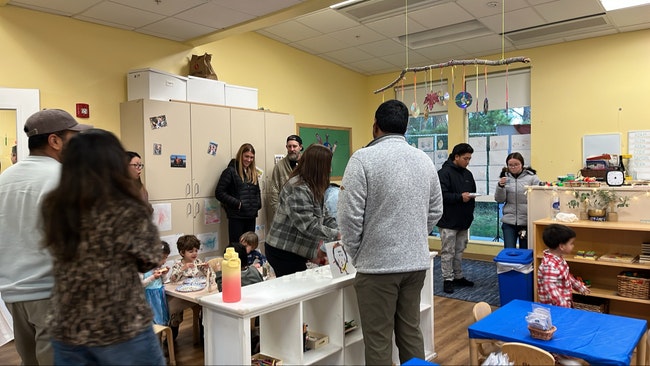 People and children in a classroom with various activities and displays.