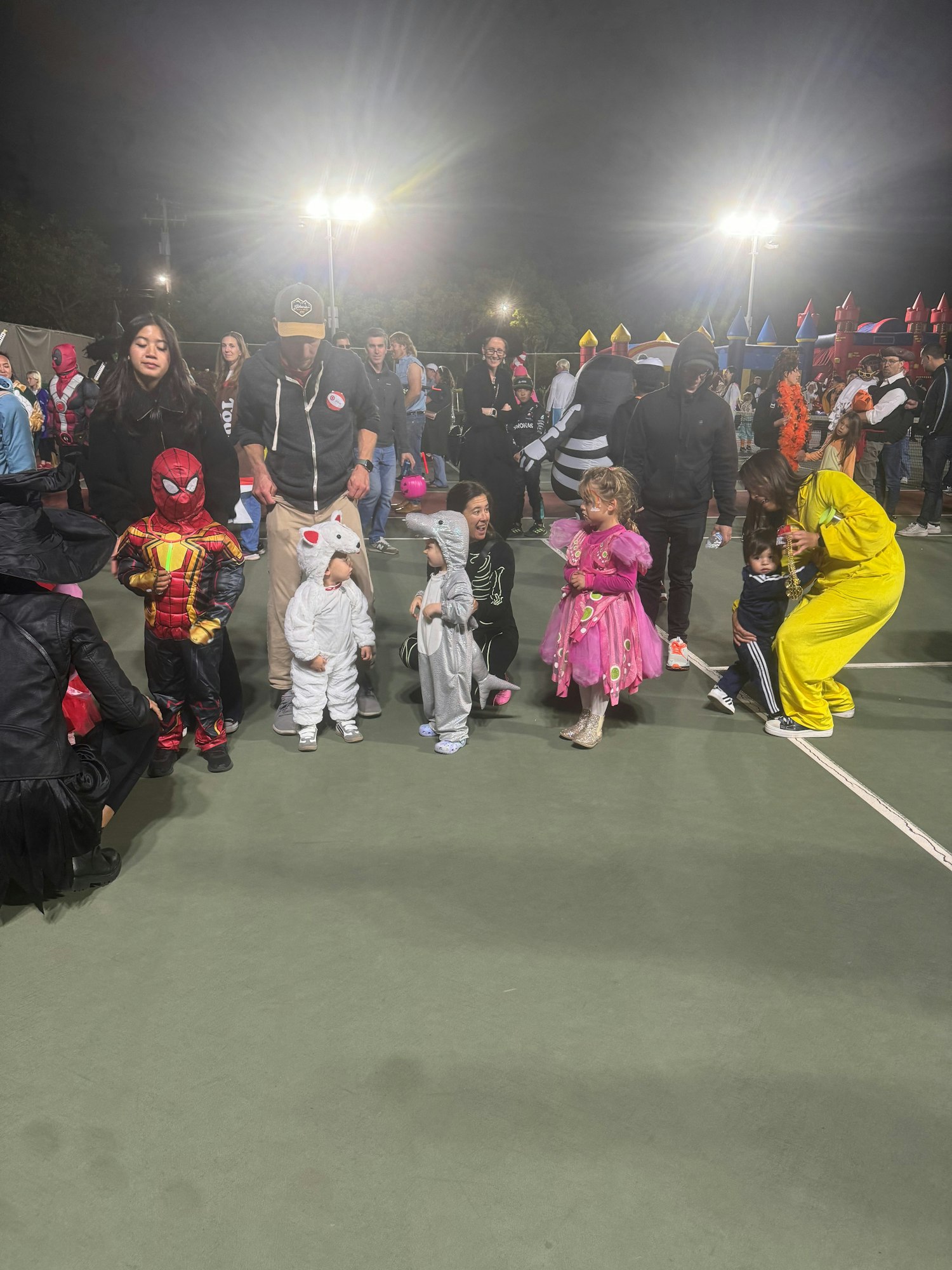 A group of adults and children, some in costumes, gathered at an event, possibly a Halloween or costume party.