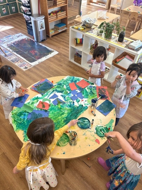 Children painting and crafting at a round table in a classroom with art supplies and paper.