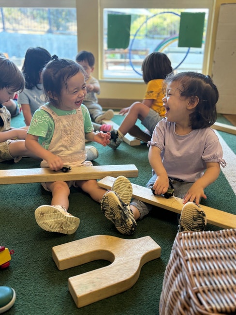 Two joyful children playing with wooden toys, laughing together in a sunny playroom.