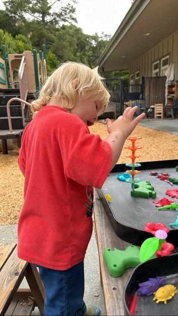 A child in a red shirt plays with colorful toys at an outdoor table.