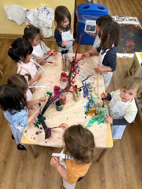Children painting together around a table filled with paint supplies and colorful artwork.