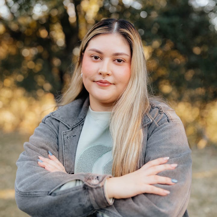 A person with long hair wearing a jacket, standing outdoors with arms crossed.