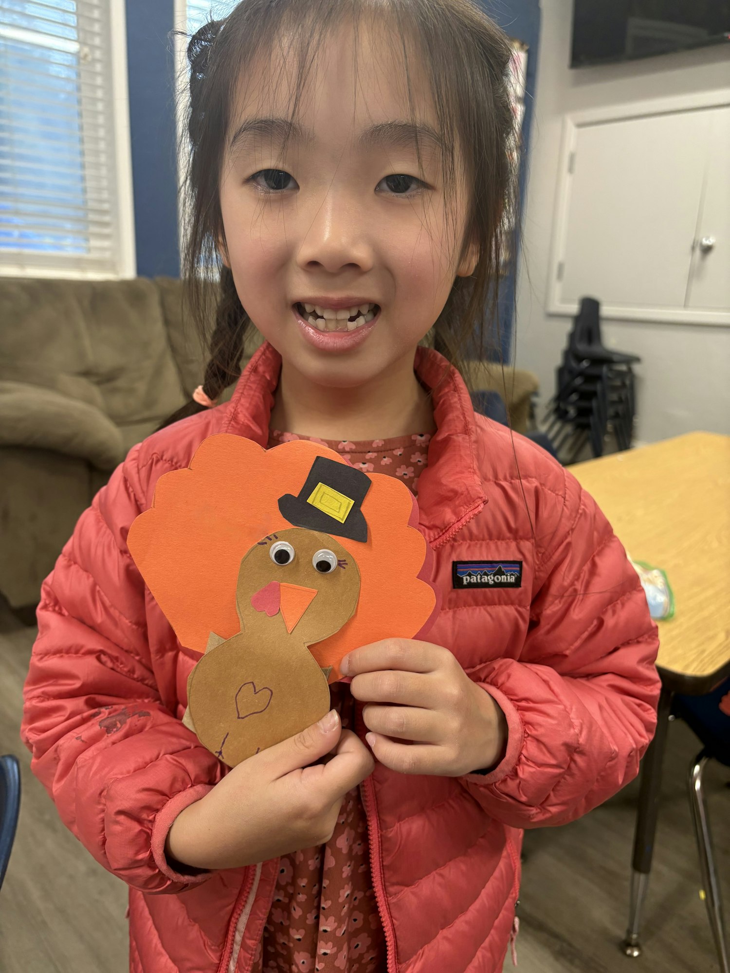 A child holding a handmade turkey craft with googly eyes and a top hat, smiling.