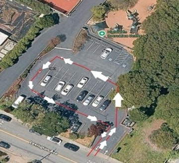 An aerial view of a parking lot with outlined driving paths and parking spots near a recreation center.