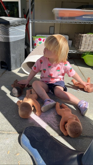 A child sitting on the ground surrounded by several baby dolls.