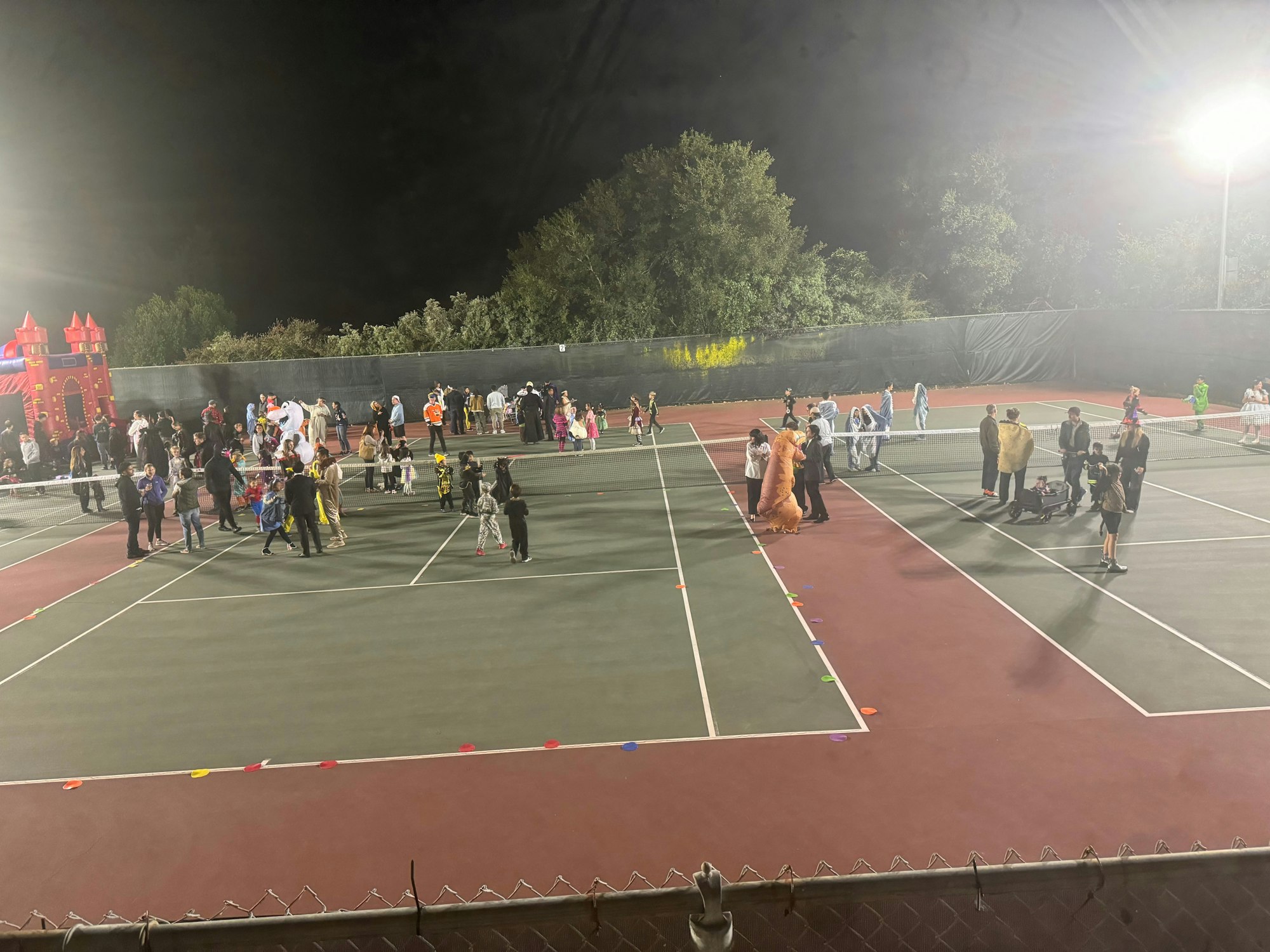 A lively outdoor event with people in costumes and an inflatable castle on a tennis court.