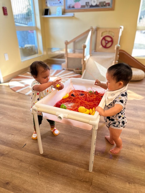 Two toddlers playing with toy balls and strings in a playroom.