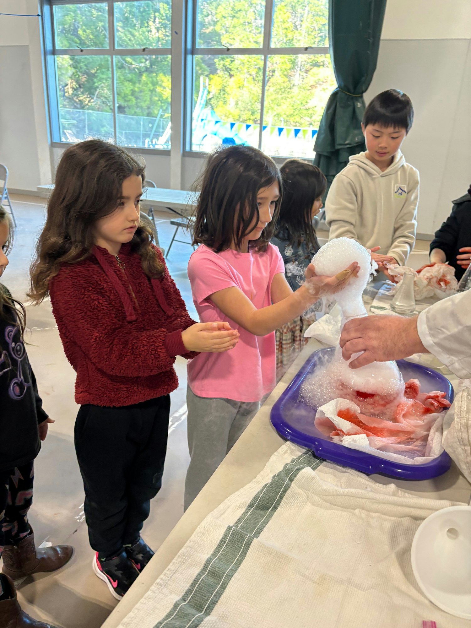 Children engaging in a science activity with a bubbling sphere and a tray on a table.