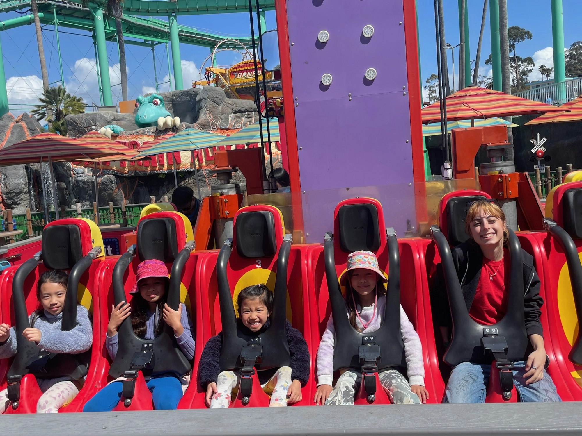 A group of people sitting in a thrilling amusement park ride with colorful seats and a dragon-themed backdrop.