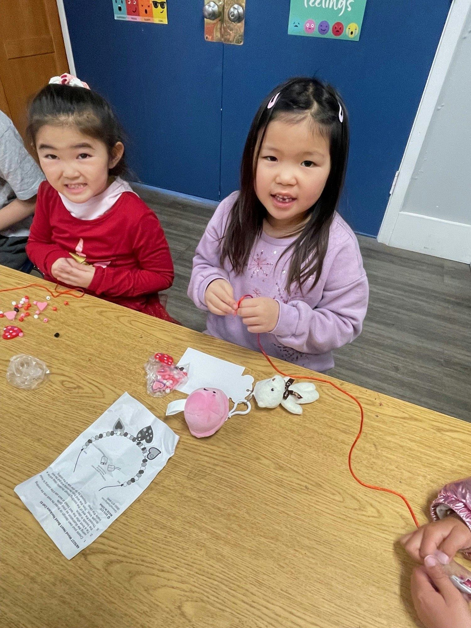 Two children at a table doing a craft activity with beads and string.