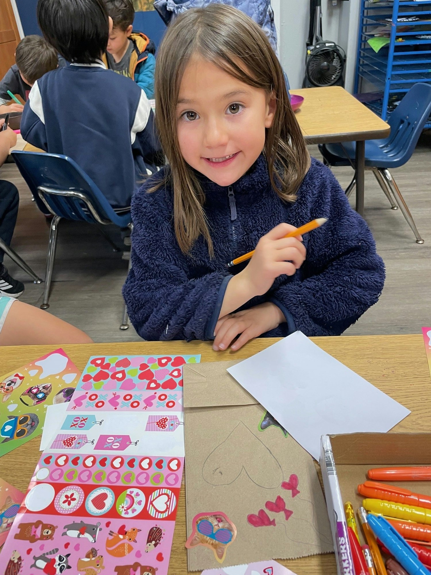 A smiling child wearing a fuzzy jacket is surrounded by stickers and markers, engaging in art and craft activities.