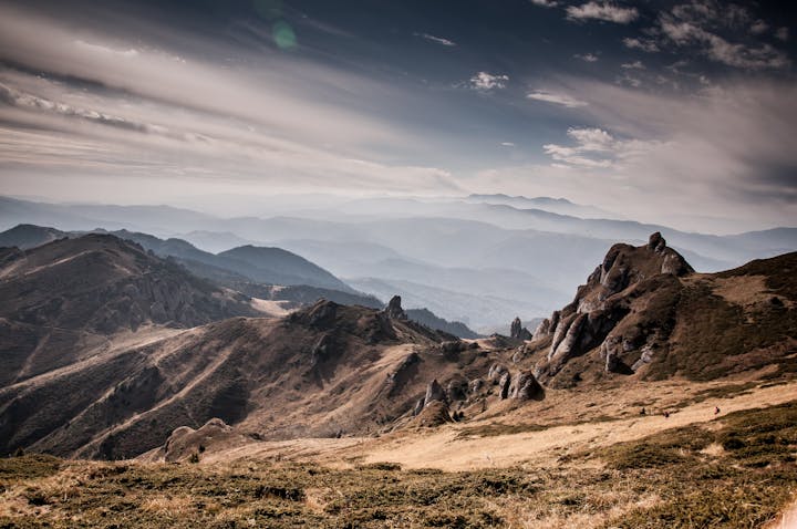 A scenic mountain landscape with rolling hills, rocky formations, and a misty atmosphere in the distance.