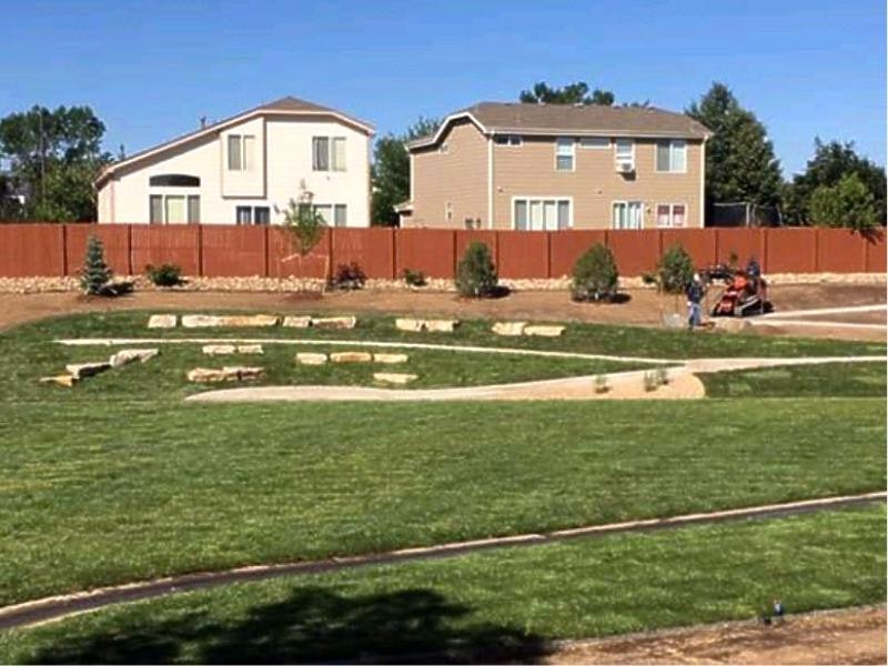A landscaped yard with a lawn cut to spell "LOVE," a pathway, trees, a wooden fence, and a person in the background.