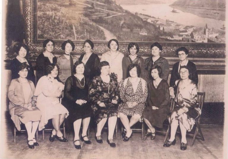 Vintage group photo of women in early 20th-century attire with a scenic backdrop.