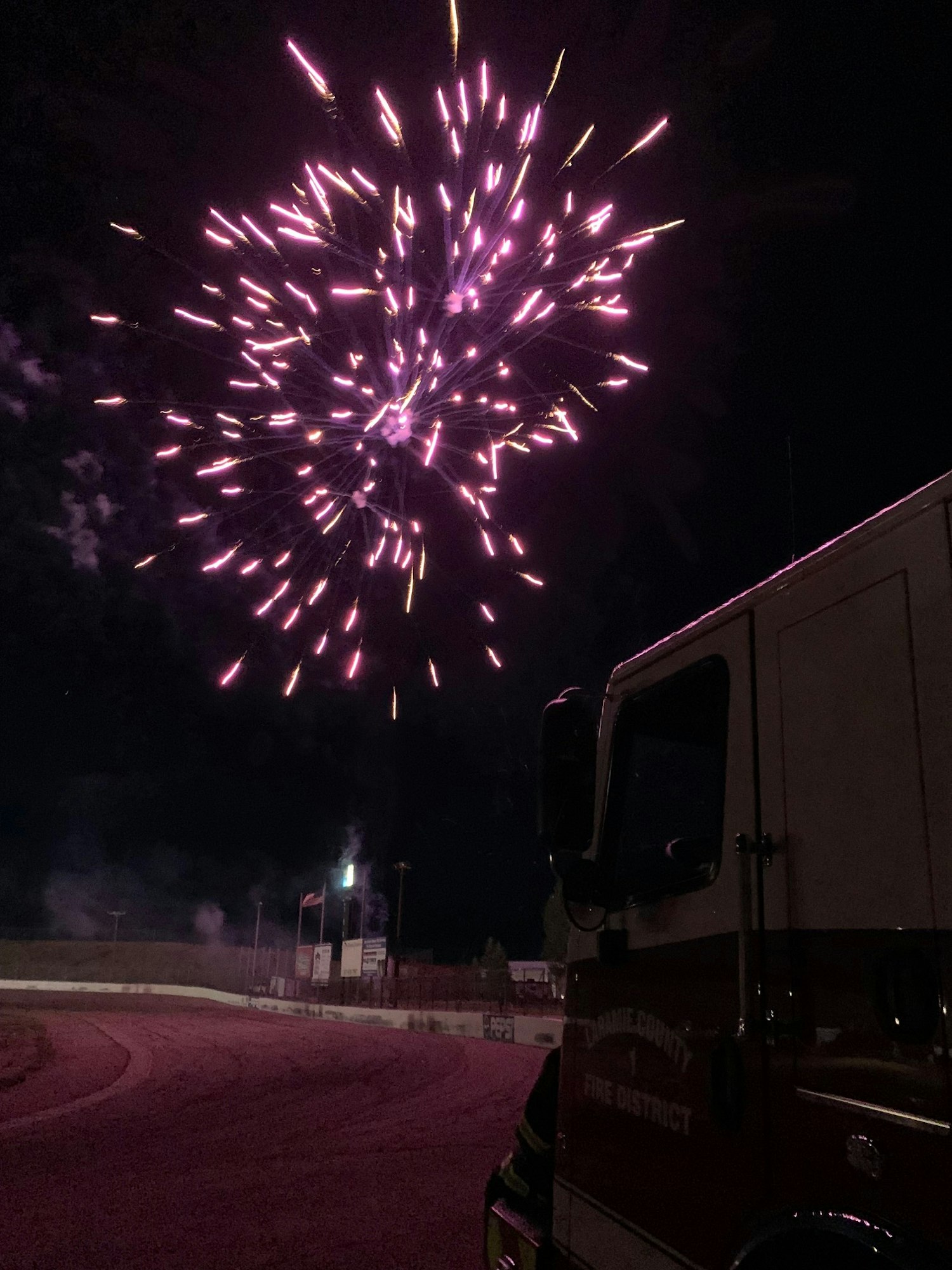 Fireworks exploding in the night sky next to a parked vehicle at a fairground.