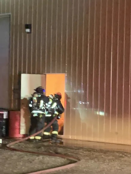 Firefighters with a hose near an orange glow, suggesting firefighting activities at night.