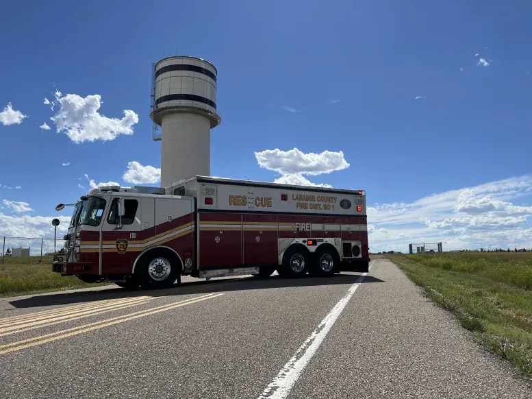 A fire truck by a road with a clear blue sky and an airport control tower in the background.