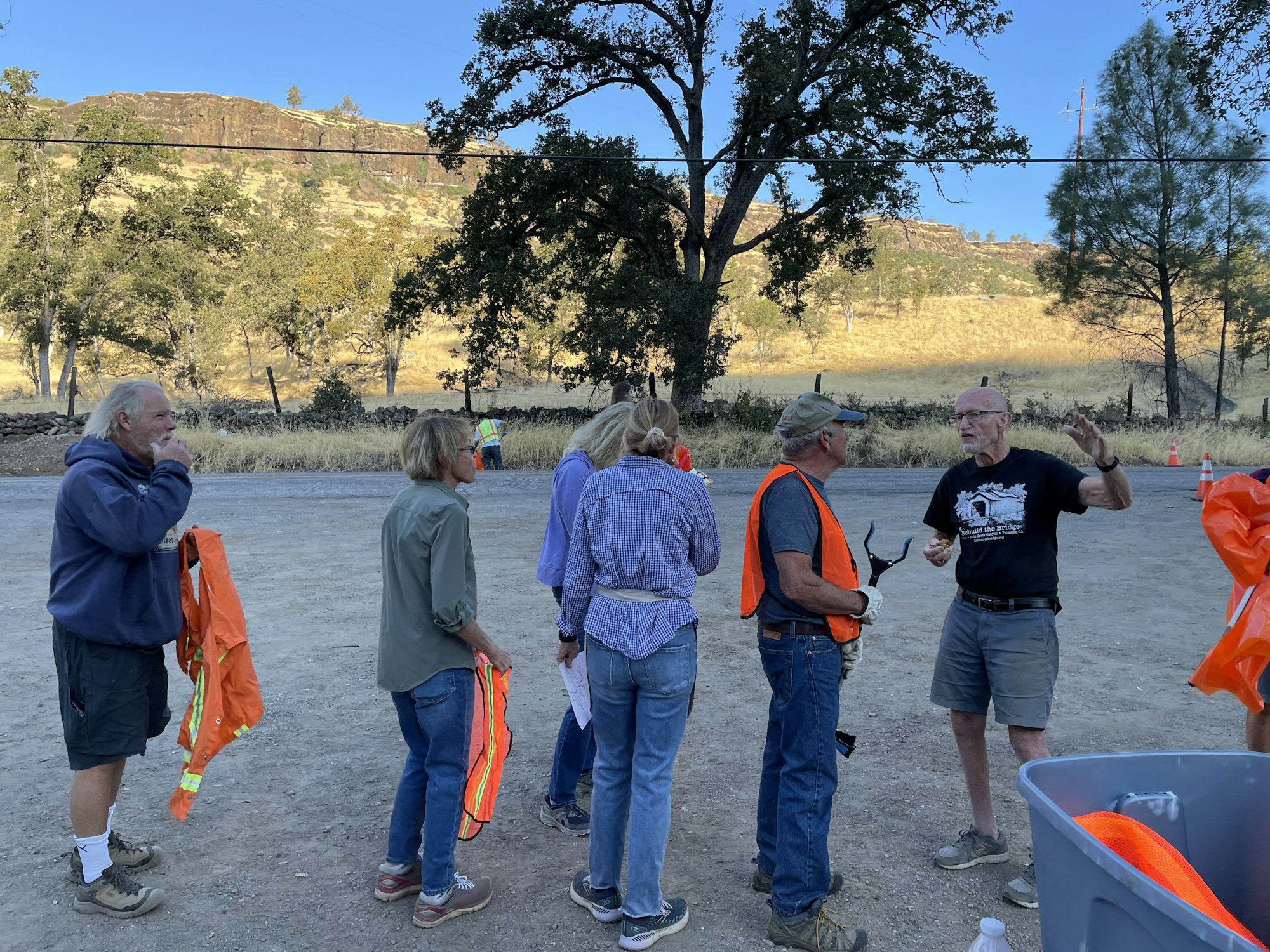 A group of people outdoors, some wearing orange safety vests, engaged in a discussion or activity.