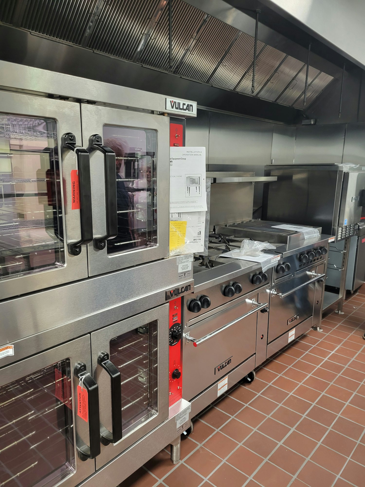 Commercial kitchen with stainless steel appliances including ovens and stovetops, brand labeled "Vulcan."