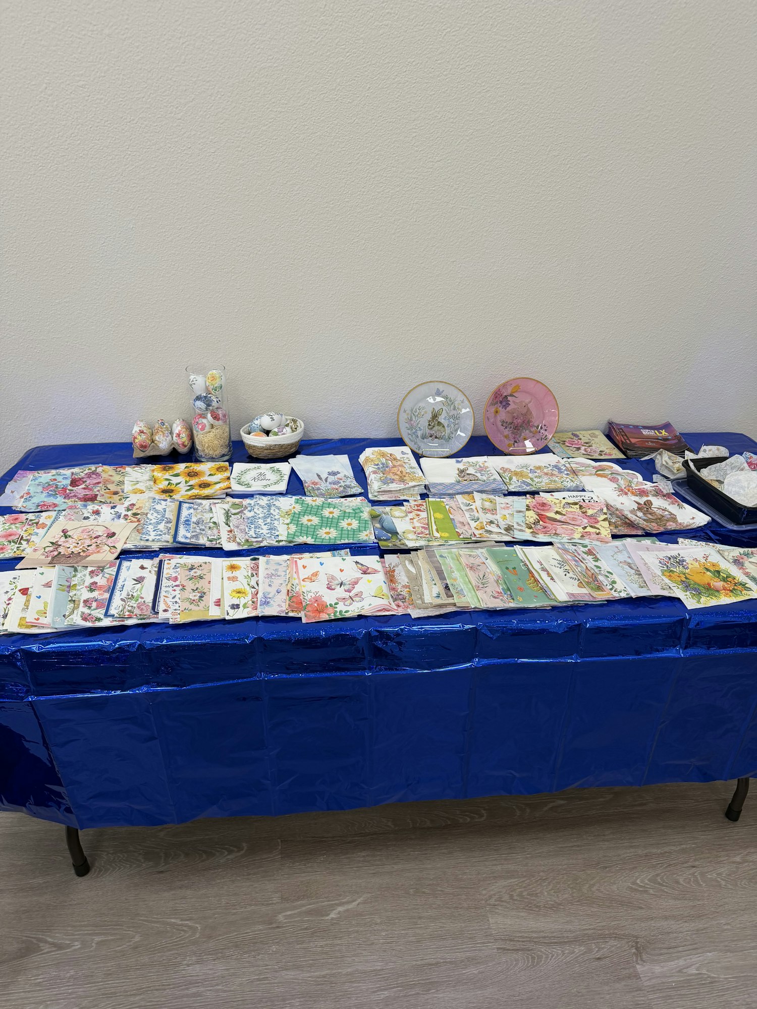 A table covered with a blue cloth displaying various decorative plates and an assortment of colorful cards and items.