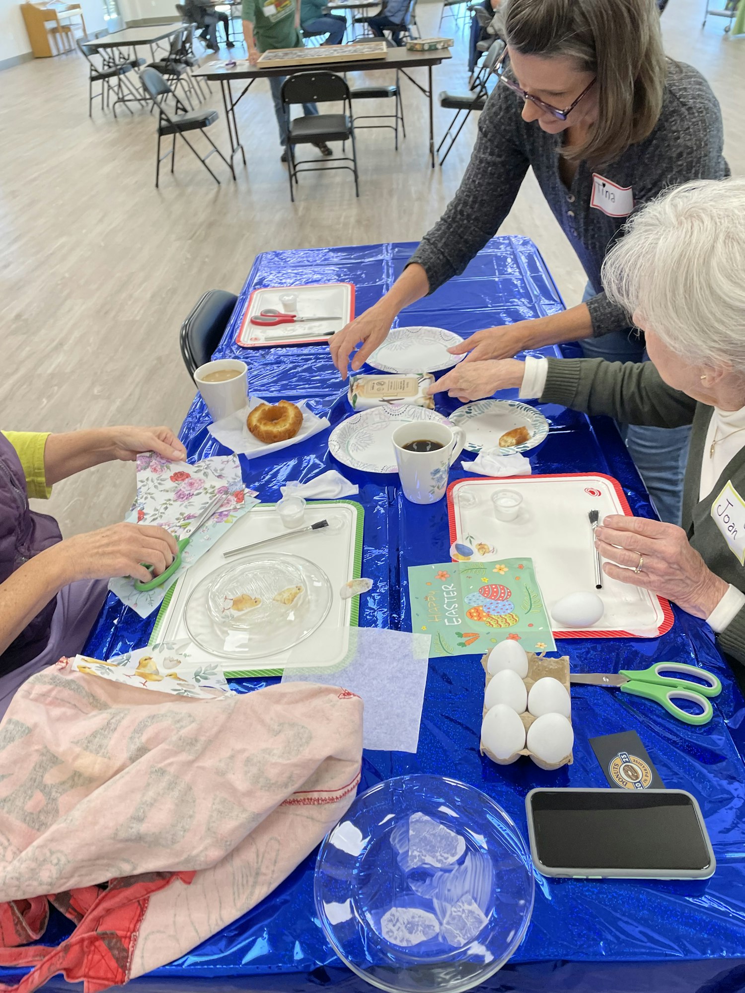 A group of people working at a table with food, eggs, and craft materials in a social setting.