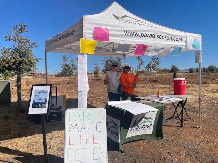 Two women stand under a tent for Paradise Recreation and Park District, promoting Lakeridge Park with a sign saying "Parks Make Life Better."