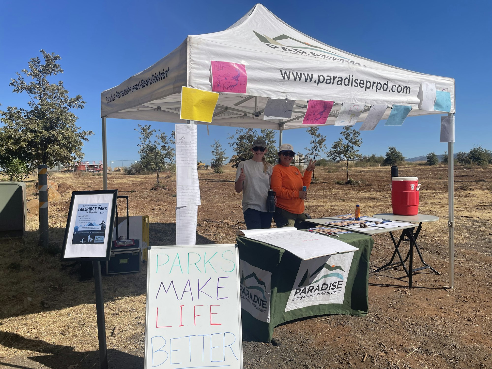 Two women stand under a tent for Paradise Recreation and Park District, promoting Lakeridge Park with a sign saying "Parks Make Life Better."