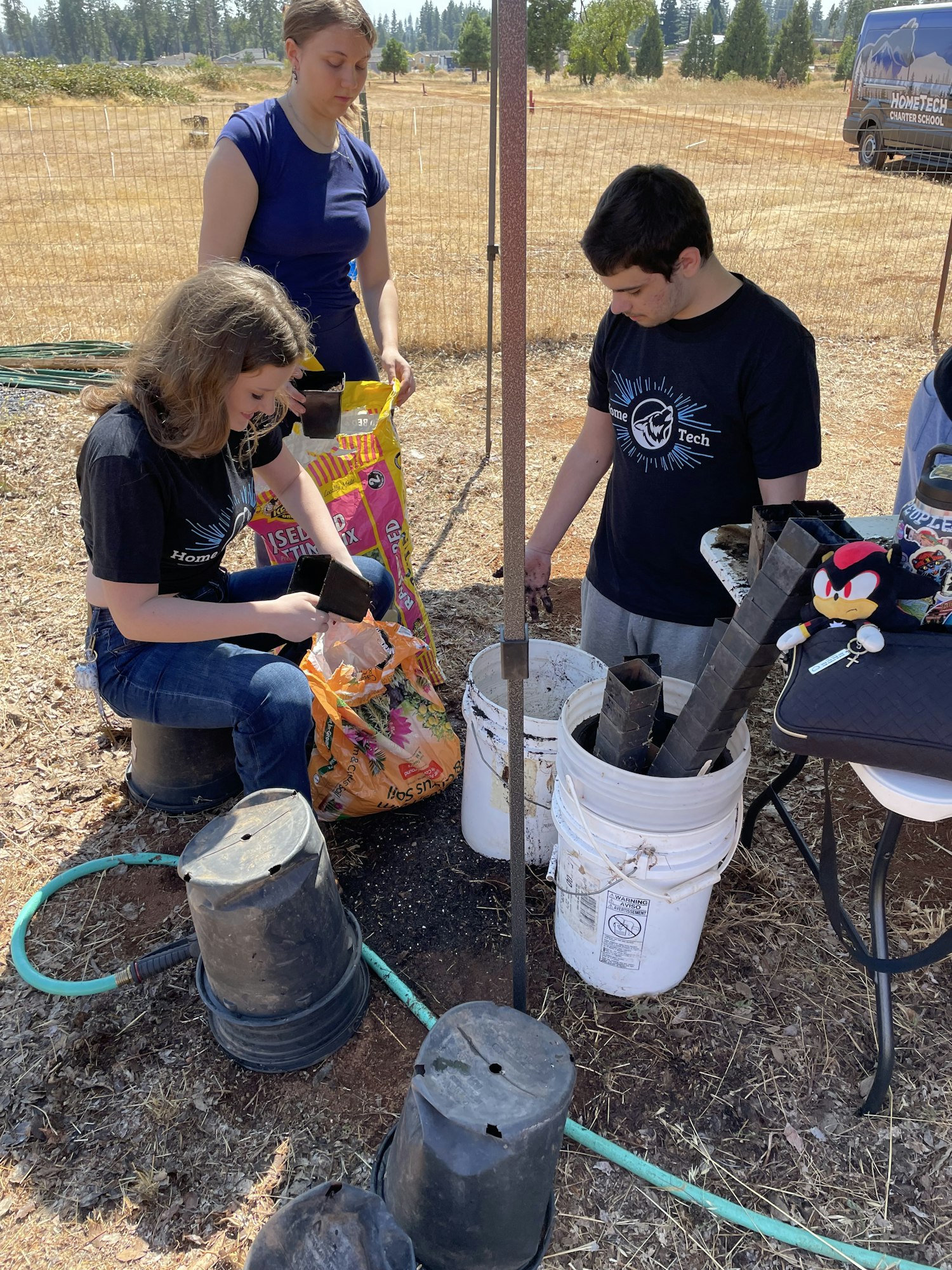 A group of people is working outdoors with pots, soil, and gardening supplies, likely preparing plants or a gardening project.