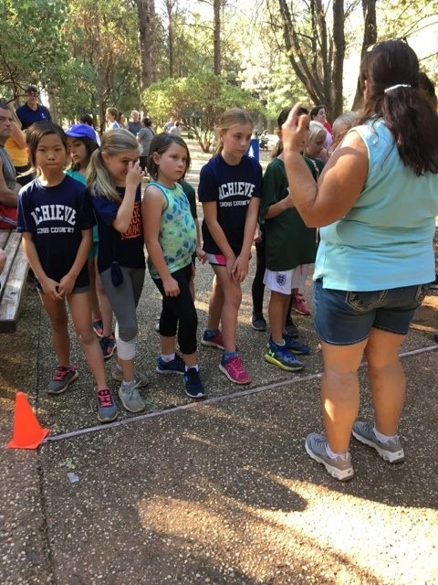 A group of children listening to an instructor outdoors, possibly a sports or camp activity.