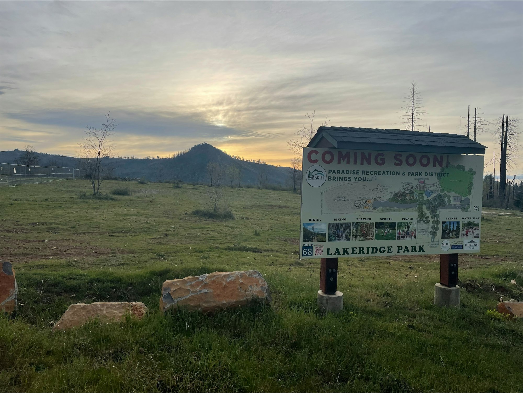A sign announces the upcoming Lakeridge Park, featuring activities like hiking, biking, sports, and picnics, set against a scenic backdrop.