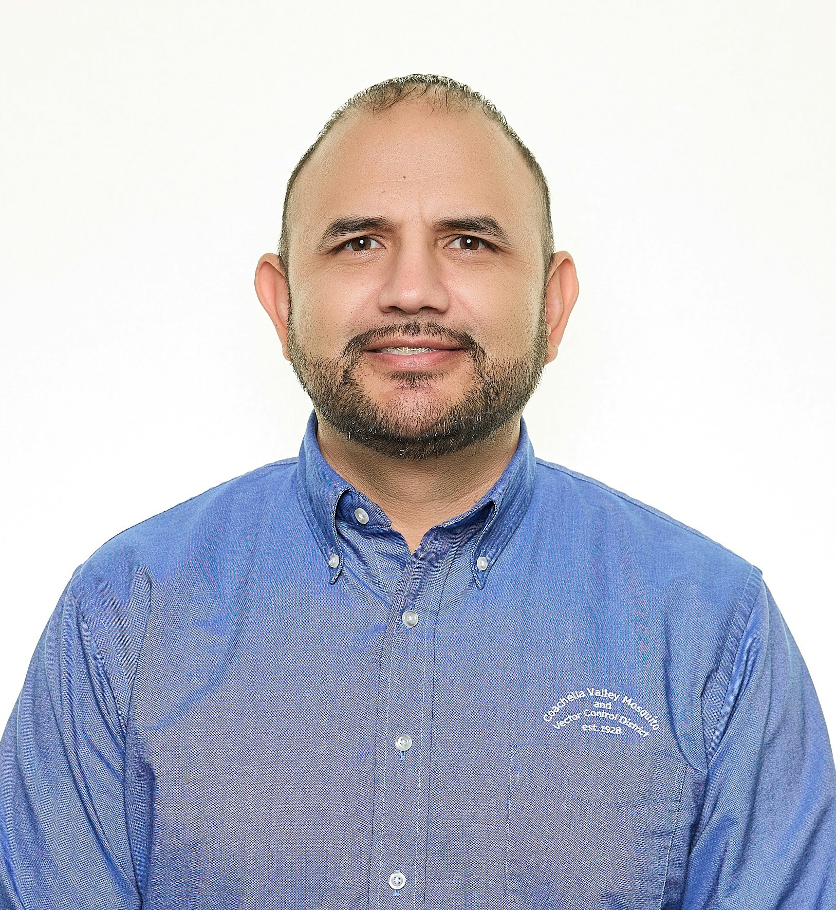A man in a blue button-up shirt with text on the pocket against a white background.