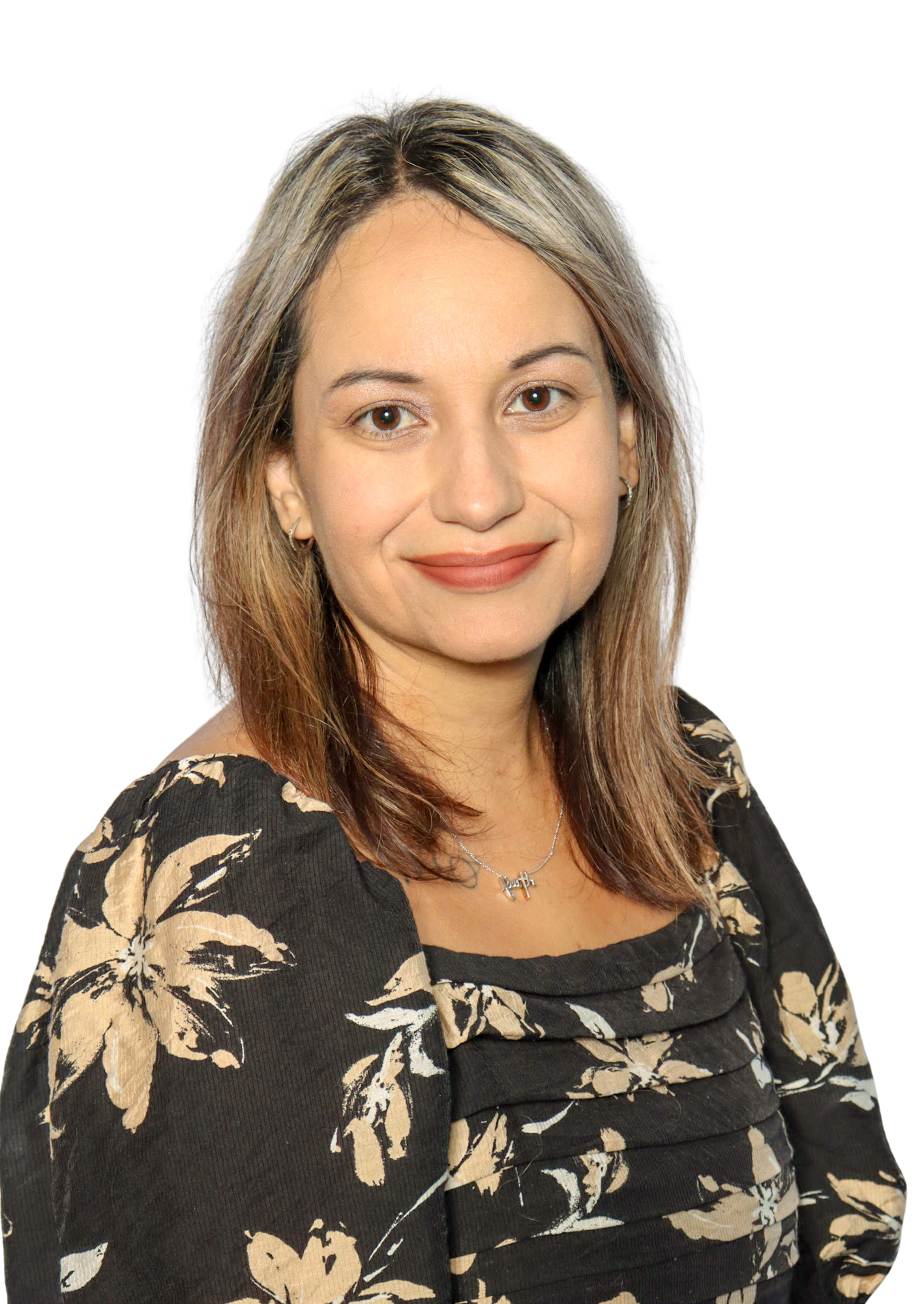 A person with shoulder-length hair, wearing a dark floral-patterned top and a necklace.