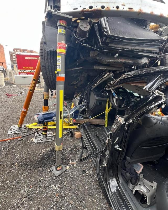 A vehicle is overturned and supported by jacks, revealing significant damage to its interior and structure.