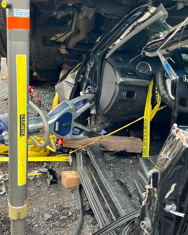A damaged black vehicle from an accident, with tools and safety equipment nearby, indicating a rescue or recovery operation.