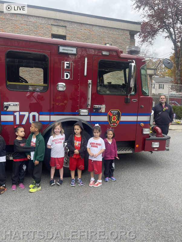 Children from Sacred Heart School stand in front of a fire truck, with a firefighter smiling nearby.