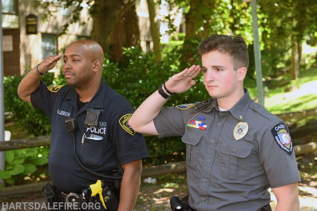 Two police officers in uniform saluting outdoors.