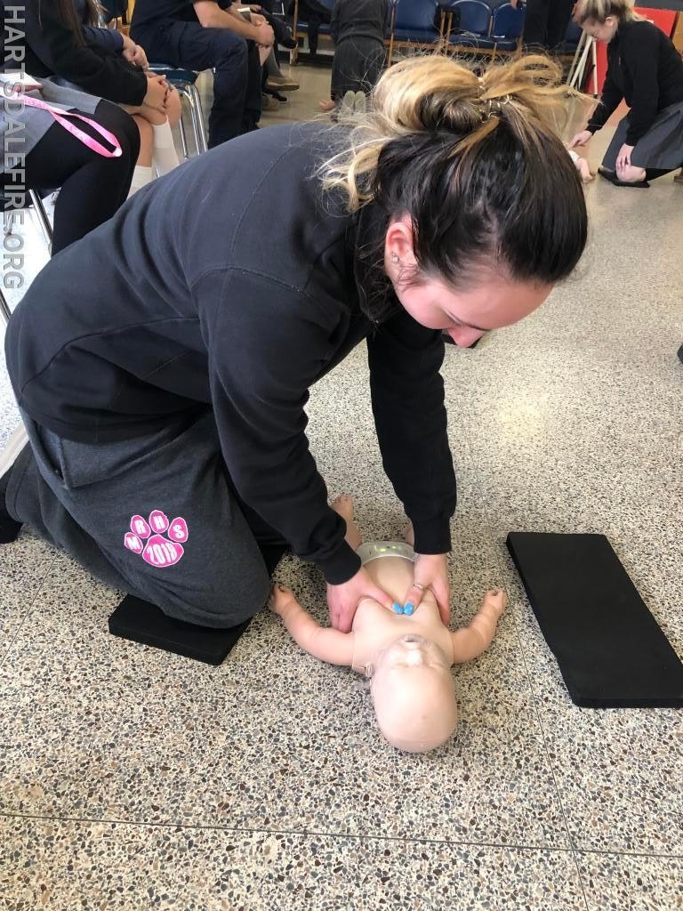 A person practicing infant CPR on a baby mannequin in a classroom setting.