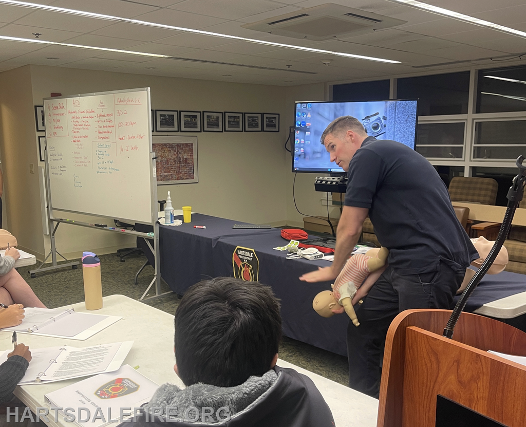 A training session on CPR or first aid, featuring an instructor demonstrating on a practice doll in front of a classroom.